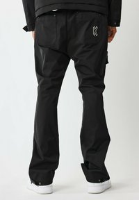 Pantaloni impermeabili neri con una vestibilità ampia, dotati di una tasca con zip, un logo ricamato sul retro e dettagli a pressione ai polsini.