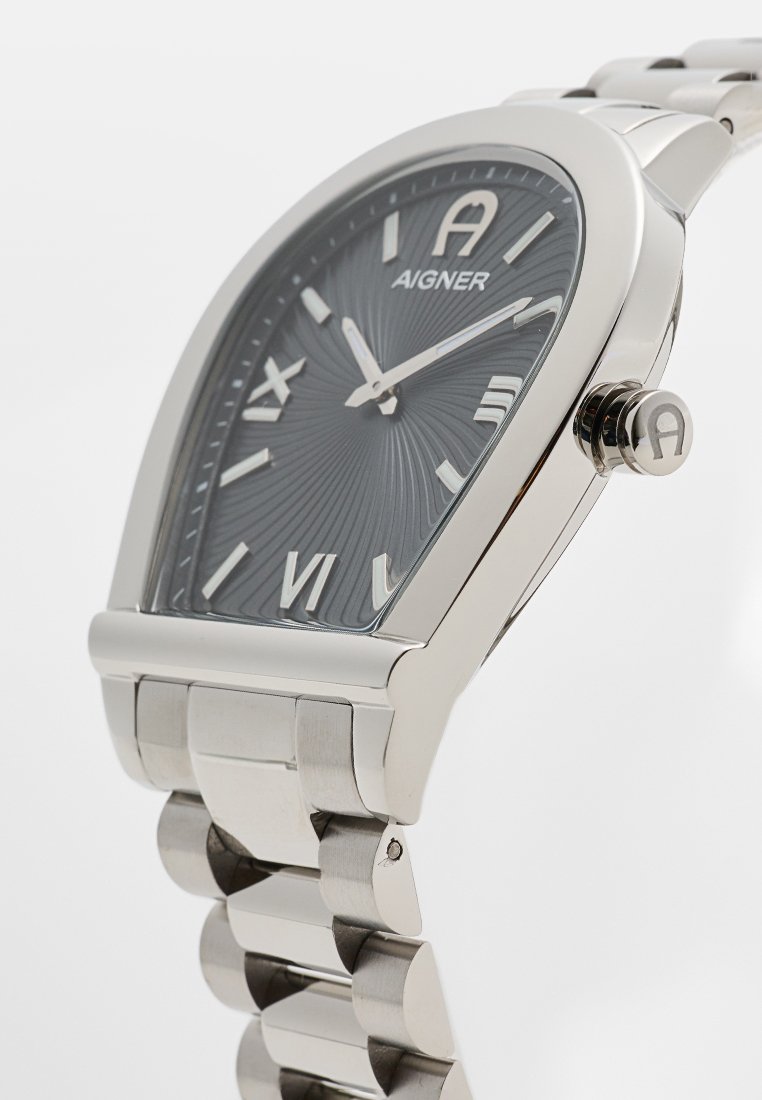 Silbernes Metallarmbanduhr mit schwarzem strukturiertem Zifferblatt, römischen Ziffern und Aigner-Logo, die die Zeit um 11:10 anzeigt.