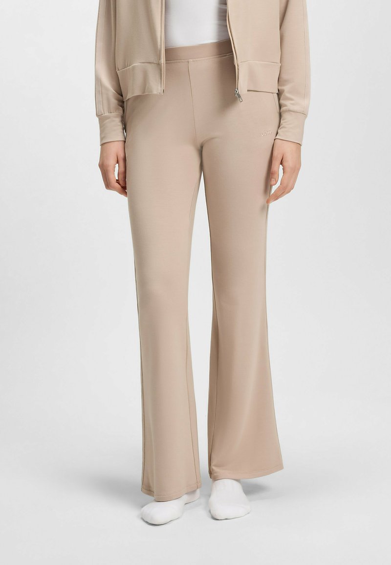 Beige flare pants gemaakt van zachte stof met een gladde textuur. Heeft een brede tailleband en een subtiele logodetail aan de zijkant.
