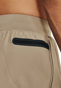 Beiga sportshorts med en svart dragkedjeficka på högra sidan och ett elastiskt midjeband för komfort. Slätt, lättviktsmaterial.