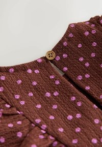 Brunt texturerat tyg med rosa prickar och en liten rund träknapp som fäster en slitsöppning.