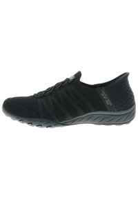 Sorte slip-on sko med elastiske stropper, teksturert stoff og en fleksibel gummisåle med sirkulære mønstre for grep.