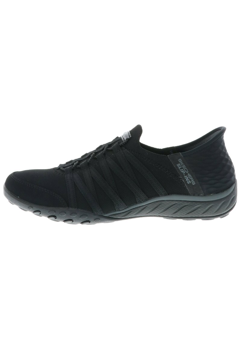 Sorte slip-on sko med elastiske stropper, teksturert stoff og en fleksibel gummisåle med sirkulære mønstre for grep.
