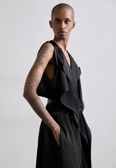 Black sleeveless dress with a wrap design, featuring ruffled accents, side pockets, and a smooth texture, highlighting body contours.