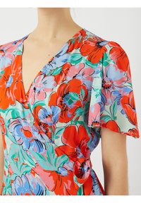 Robe portefeuille florale avec des manches bouffantes courtes. Présente un motif de fleurs rouges, roses et bleues sur un fond vert clair. Tissu texturé.