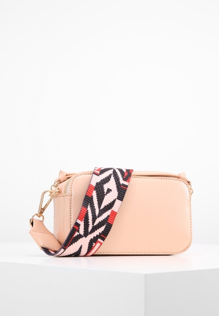 Persikofärgad läderaxelväska med ett geometriskt mönstrat band i svart, röd och vit. Har en rektangulär form och detaljer i guld.