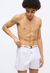 Άσπρα ριγέ μποξέρ με ελαστική μέση σε ναυτικό μπλε χρώμα με λογότυπο, διαθέτουν κλείσιμο με κουμπιά μπροστά και άνετη εφαρμογή. Είναι ορατό το υφασμένο ύφασμα.