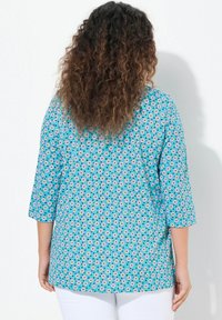 Türkise Bluse mit floralem Muster, 3/4-Ärmeln und lockerer Passform. Der Stoff hat eine glatte Textur und eignet sich gut für die Freizeit.
