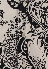 Primer plano de una tela con un patrón floral en blanco y negro y abstracto, con botones blancos en la parte frontal de una camisa.