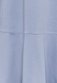 Ljusblå klänning med en jämn textur, en utsvängd kjol och en sömdetalj över midjan, tillverkad av mjukt tyg.