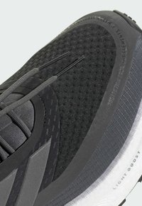 Black running shoe with textured mesh upper, reinforced accents, patterned laces, and a light gray outsole featuring 'LIGHT BOOST' detail.