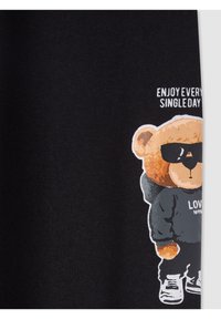 Miś ubrany w okulary przeciwsłoneczne, bluzę z kapturem i sneakersy, z napisem "Ciesz się każdym dniem" na czarnym tle.