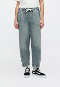 Pantaloni din denim bleu deschis, lejeri, cu talie elastică și buzunare frontale. Asortați cu teniși negri și albi.