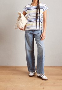 Pruhované tričko s krátkým rukávem v bílé, modré a žluté barvě, spárované s světle modrými širokými džínami a bílými teniskami s černými pruhy.