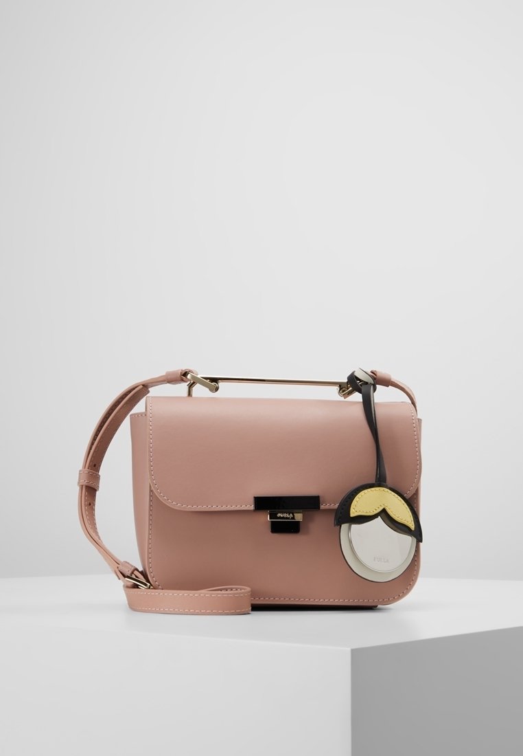 Růžová kožená kabelka přes rameno s klopou, zlatými doplňky a kulatým přívěskem s černými a žlutými akcenty. Hladký povrch, obdélníkový tvar.