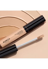 Anti-cernes Full Coverage de KIKO Milano avec un tube beige et un bouchon noir, doté d'une embout applicateur doux, sur un fond beige clair.