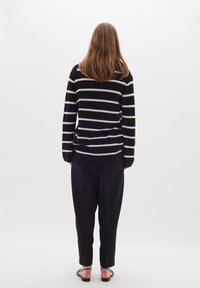 Svart och vit randig tröja med långa ärmar, tillsammans med lösa svarta byxor och svarta sandaler, sedd bakifrån.