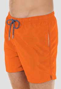 Oranssit uimapuvut, joissa on nauhalla säädettävä vyötärö. Mukana kontrastiväriset ompeleet ja sivutasku. Sujuva, kevyt materiaali.