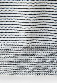 Gros plan sur un tissu tricoté blanc avec des rayures horizontales noires alternant fines et épaisses et des motifs de couture texturés.