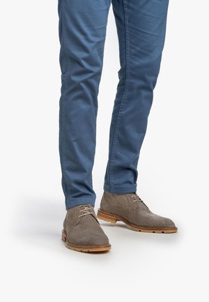 Botas de cordones de textura marrón claro con suela de goma beige, combinadas con pantalones de algodón azul de corte slim.