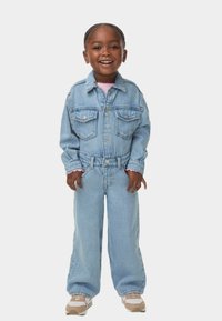 Lichtblauwe denimjack met twee borstzakken en bijpassende wijde jeans. Inclusief een roze shirt en beige sneakers met witte accenten.
