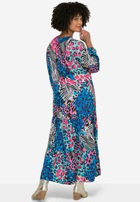 Robe maxi avec des motifs multicolores vibrants, dont des imprimés léopard et zèbre bleus, roses et noirs ; design à volants ; manches longues.