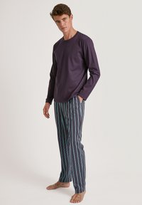 Pyjamセット met een paarse top met lange mouwen en meerkleurige gestreepte broeken met blauwe, groene en witte lijnen op een donkere achtergrond.