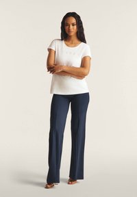 Valkoinen lyhythihainen t-paita, jossa on "FREDDY" -painatus, yhdistettynä laivastonsinisiin leveälahkeisiin housuihin. Varustettu sileällä pinnalla ja rentouttavalla istuvuudella.