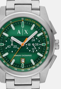 Ura iz nerjavečega jekla s zelenim številčnico, belimi oznakami, oranžnimi detajli, kronografski pod številčnici ter oknom za datum na položaju 6. ure.