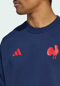 Marineblauwe sweatshirt met een grafisch ontwerp van een rode haan en een contrasterend rood Adidas-logo bestaande uit drie diagonale strepen. Van katoen materiaal.