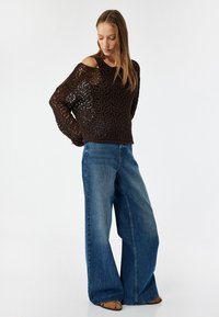 Brun hækletrøje med åben strikdesign, parret med brede blå jeans. Looket er fuldendt med lysebrune sandaler.