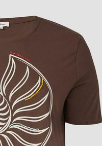 Bruine T-shirt van zachte stof met ronde halslijn, voorzien van een wit bladdesign en kleurrijke kraalaccenten in rood, geel en blauw.
