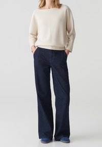 Maglione bianco a costine e jeans blu scuri larghi. L'insieme presenta una silhouette rilassata con una texture confortevole. Le scarpe blu completano il look.