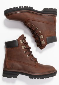 Botas de cuero marrón con acentos negros, punta redonda, ojales metálicos y cordones. Presentan una suela resistente con surcos pronunciados para mayor tracción.