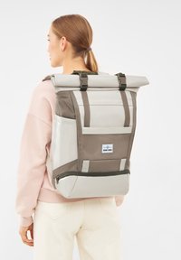 Szürke és barna, tartós anyagból készült, roll-top hátizsák. Állítható pántokkal, cipzáras zsebbel és oldalsó logóval rendelkezik.