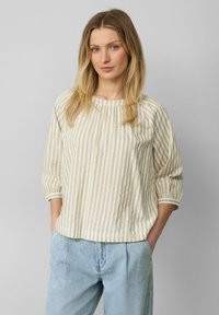 Blouse rayée beige et blanche avec un col rond, des manches trois-quarts et une coupe ample, associée à un pantalon en denim bleu clair.