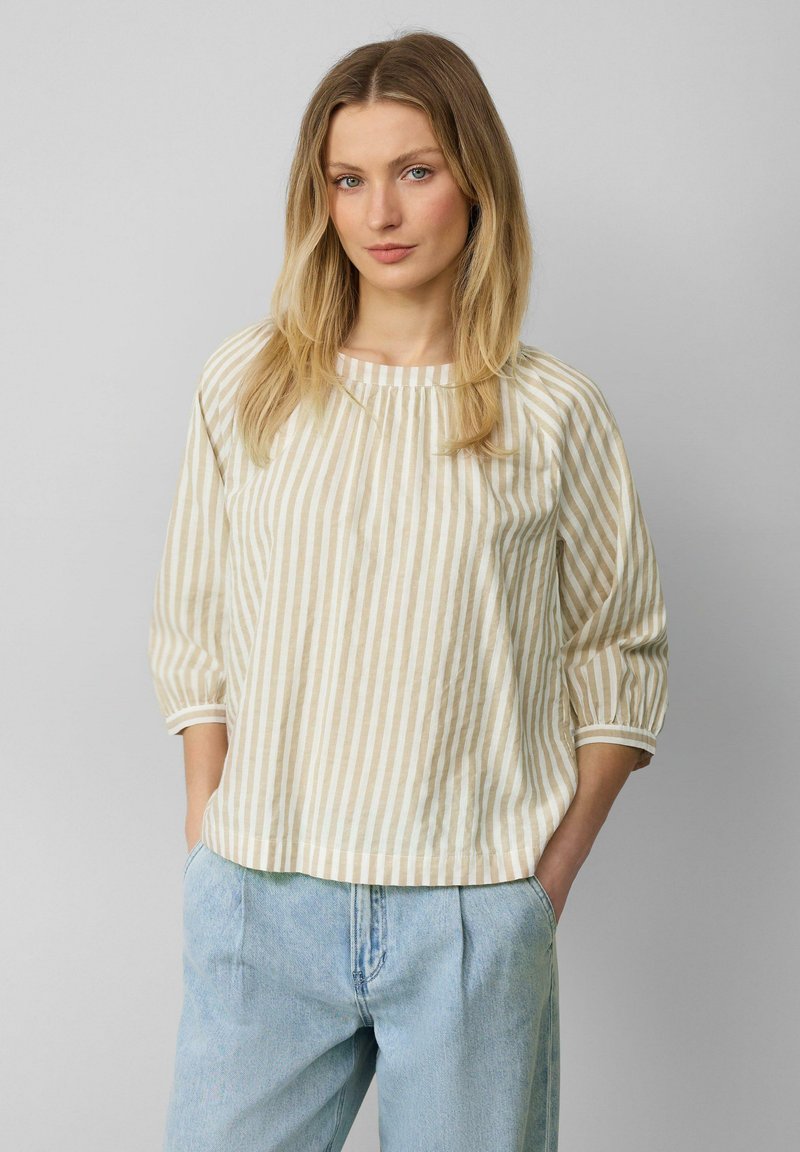 Blouse rayée beige et blanche avec un col rond, des manches trois-quarts et une coupe ample, associée à un pantalon en denim bleu clair.