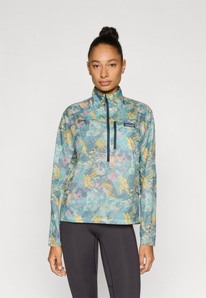 Let og lynlåspullover med høj krave, der har et blomsterprint i blå, gul og pink på et tekstureret stof.