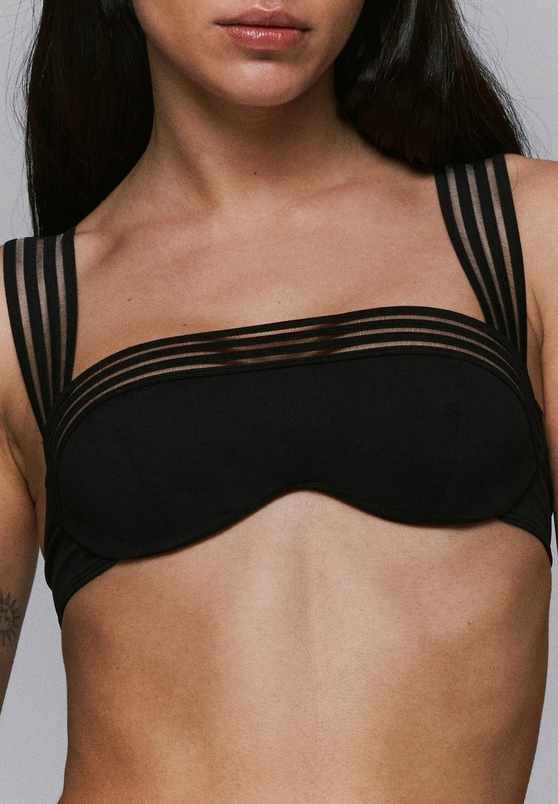 Sostenes negro con un diseño estructurado, que presenta tirantes anchos y прозрачных con rayas horizontales, tejido suave y una forma lisa y contorneada.