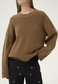 Maglione a coste marrone con maniche lunghe e dettagli orlo sfrangiato. Abbinato a pantaloni neri con accenti in grommet argentato.