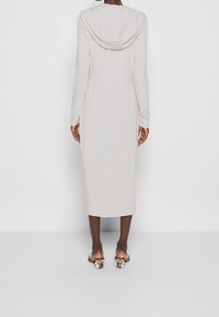 Lång, huvad klänning i ljusgrått tyg med långa ärmar, avslappnad passform och midilängd. Bärs med klacksandaler.