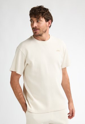 Lichtbeige T-shirt met korte mouwen en wafelstructuur, een ronde hals en een subtiel logodetail, gecombineerd met bijpassende broek.