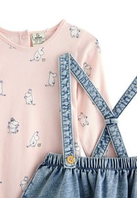 Rosa Langarmtop mit Moomin-Charakterdruck, kombiniert mit Latzhose aus Denim mit verstellbaren blauen Trägern und einem Holzkneipp-Detail.