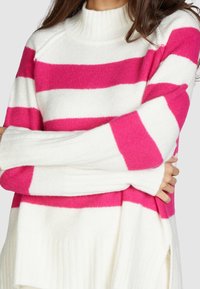 Pull en maille avec des rayures horizontales roses et blanches, col montant côtelé et manches longues. Texture douce et coupe décontractée.