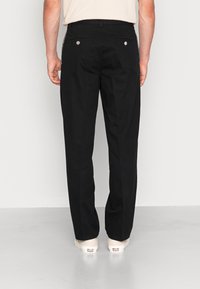 Black, straight-leg trousers made of cotton blend. Features two back pockets with silver hardware and subtle side stripes.