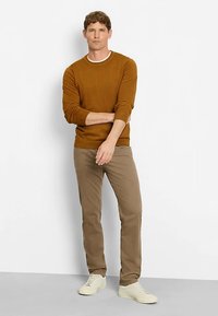 Brown knitted sweater with a round neckline, paired with beige chinos and light-colored sneakers. Neutral background.
