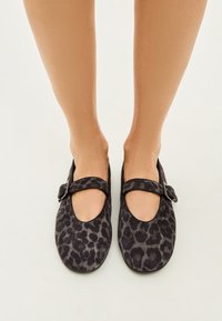 Black and gray leopard print ballet flats with a rounded toe and a single adjustable strap across the vamp. Soft suede-like texture.