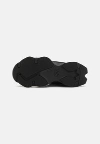 Suela de zapato atlético negro con goma texturizada para agarre, que presenta un patrón de zigzag y un corte central para flexibilidad. Logo de la marca grabado en la superficie.