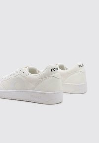 Baskets blanches en toile et en daim, avec une texture lisse, un bout rond, une épaisse semelle en caoutchouc blanc et des accents de logo noir au talon.