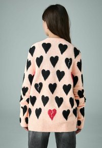 Mīksts rozā džemperis ar lieliem melniem sirds rakstiem, ar vienu sarkanu salauztas sirds detaļu apakšā, ar ribotiem piedurknēm un apmalēm.